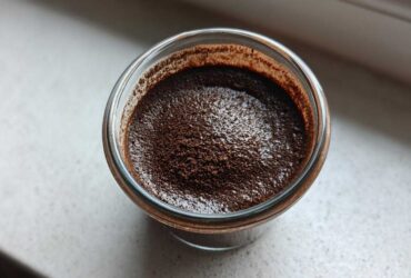 Overhead close-up of rich homemade chocolate pudding dusted with cocoa powder in a small glass jar.