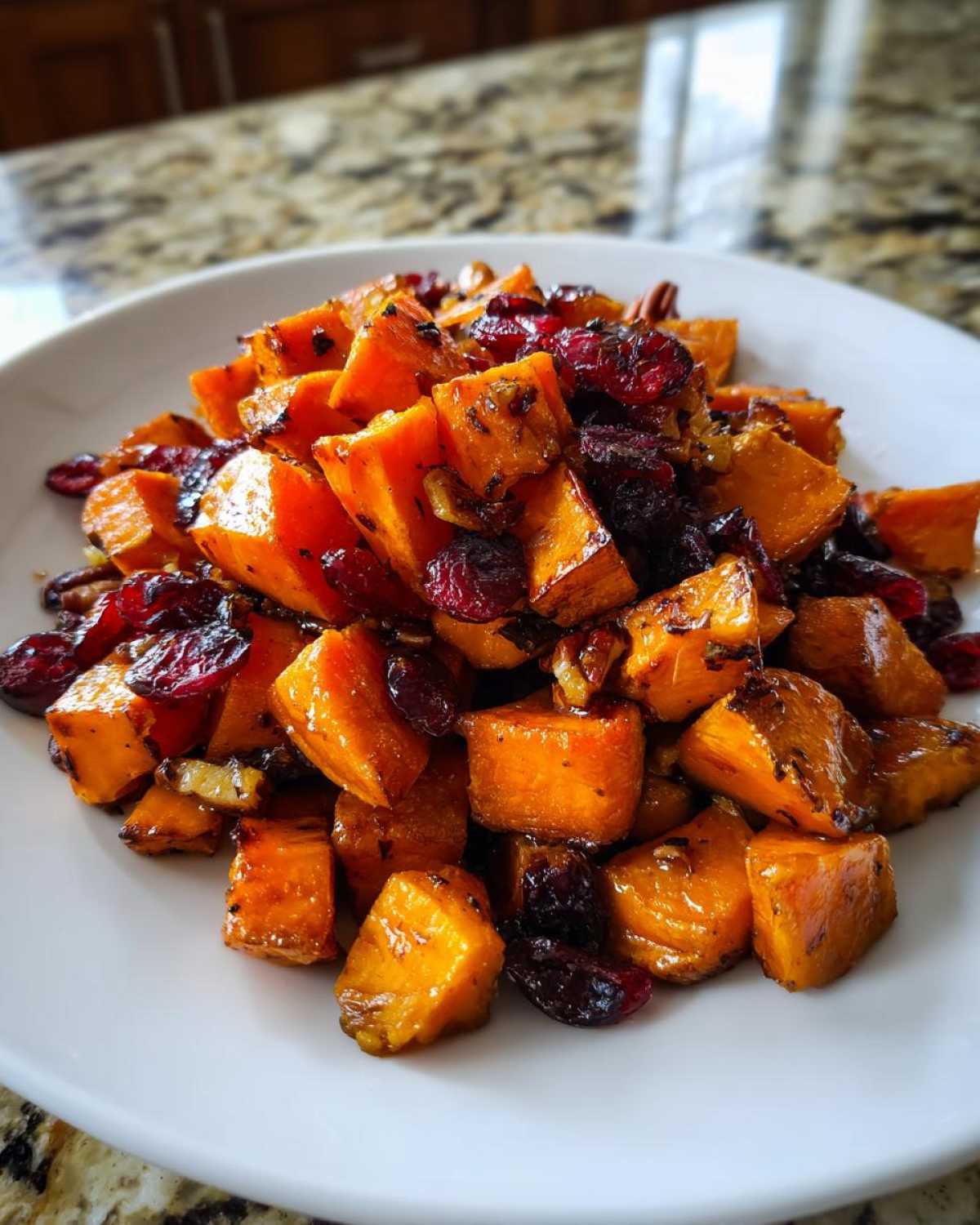 Close-up of vibrant orange roasted sweet potato salad mixed with dried cranberries and pecans on a white plate.