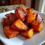 A close-up of caramelized, glazed roasted sweet potatoes cubes piled on a white plate.