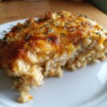 A close-up of a hearty slice of baked chicken and rice casserole topped with melted, browned cheese and fresh thyme.