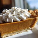 A close-up of a slice of rich, orange-colored butterscotch pie topped generously with whipped cream.