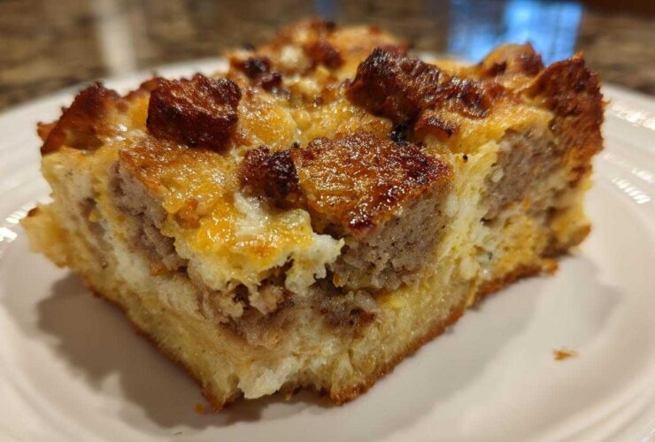 Close-up of a square slice of savory Christmas breakfast casserole featuring bread, egg, cheese, and browned sausage chunks.