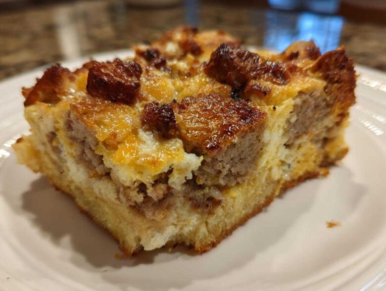 Close-up of a square slice of savory Christmas breakfast casserole featuring bread, egg, cheese, and browned sausage chunks.