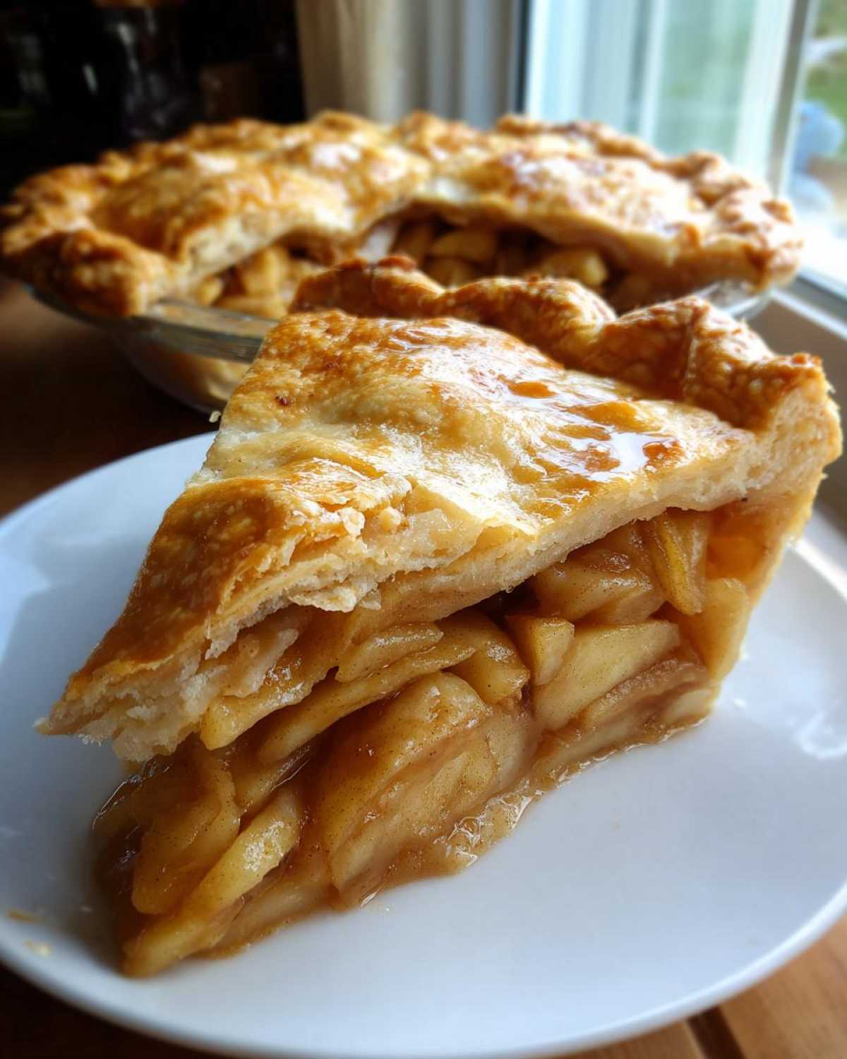 A thick slice of homemade apple pie showing layers of spiced apples and flaky crust on a white plate.