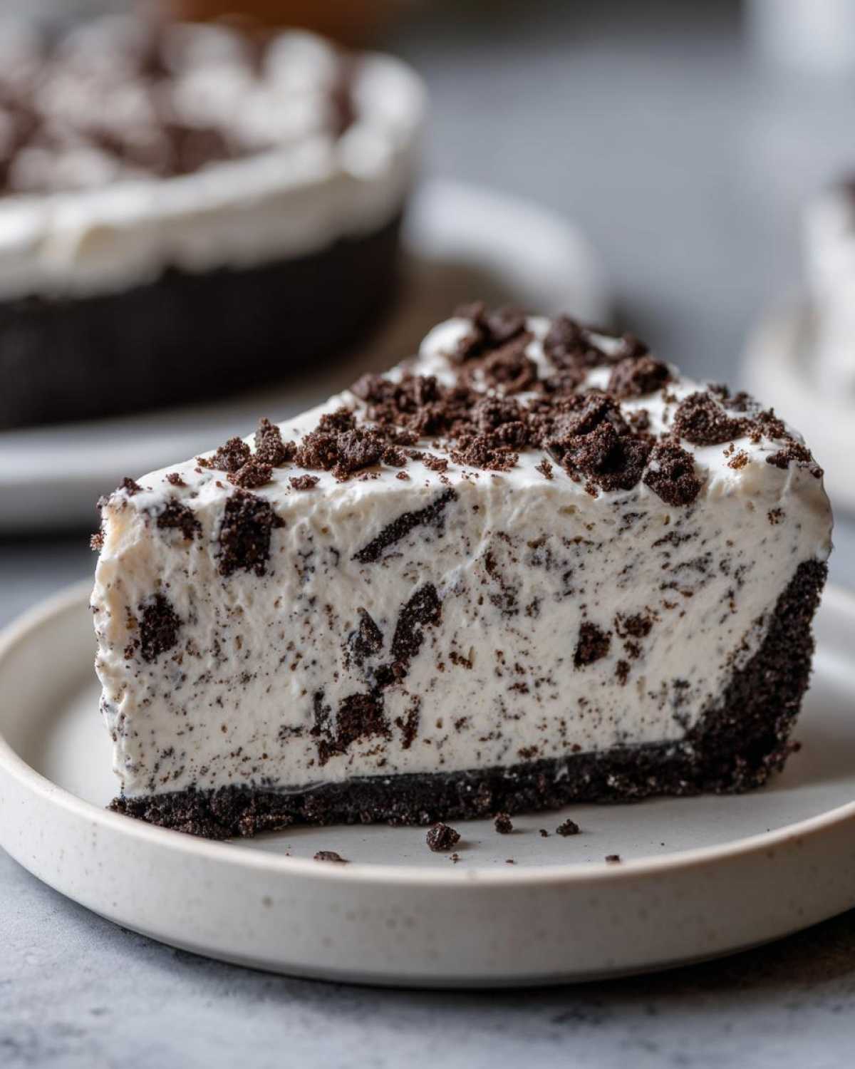 A close-up of a creamy slice of no-bake oreo pie showing the dark cookie crust and white filling studded with cookie pieces.