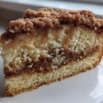 Close-up of a moist slice of coffee cake showing layers of cake, cinnamon swirl, and thick crumb topping.