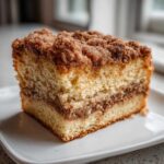 Close-up of a moist slice of coffee cake showing layers of cake, cinnamon filling, and a thick, crumbly streusel topping.