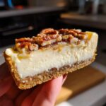 Close-up of a thick slice of pecan cream pie held up, showing the creamy filling and pecan topping.