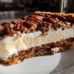 Close-up of a slice of pecan cream pie showing a graham cracker crust, pecan layer, creamy filling, and whipped topping with pecans.