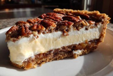 Close-up of a slice of pecan cream pie showing a graham cracker crust, pecan layer, creamy filling, and whipped topping with pecans.