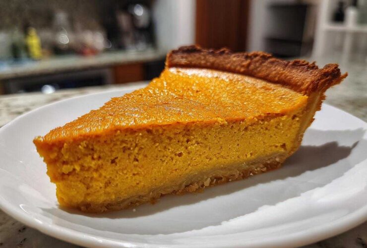 A close-up of a perfect slice of rich, orange vegan pumpkin pie on a white plate.