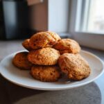 A stack of soft, golden brown applesauce cookies piled high on a white plate near a window.