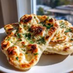 Close-up of freshly made, soft naan bread pieces topped with melted butter and chopped green herbs.