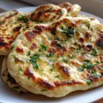 Close-up of several pieces of soft naan bread, brushed with butter and sprinkled with fresh green parsley.
