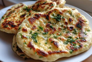 Close-up of several pieces of soft naan bread, brushed with butter and sprinkled with fresh green parsley.