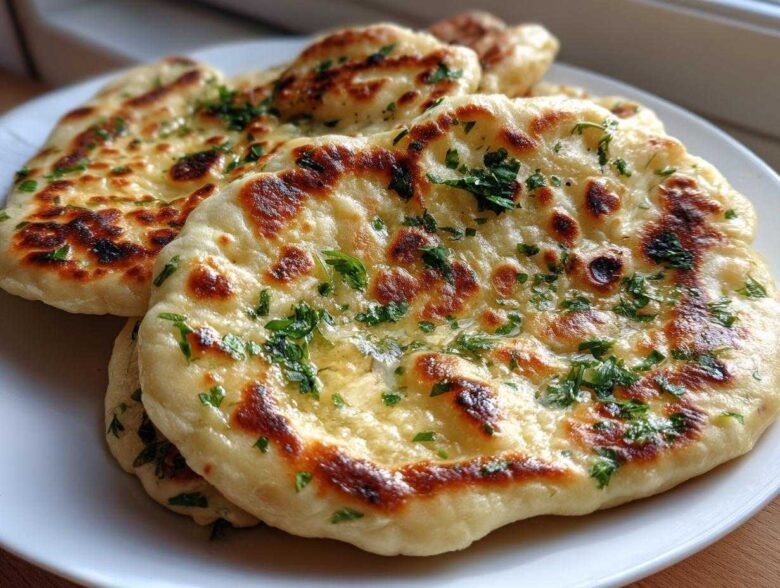 Close-up of several pieces of soft naan bread, brushed with butter and sprinkled with fresh green parsley.