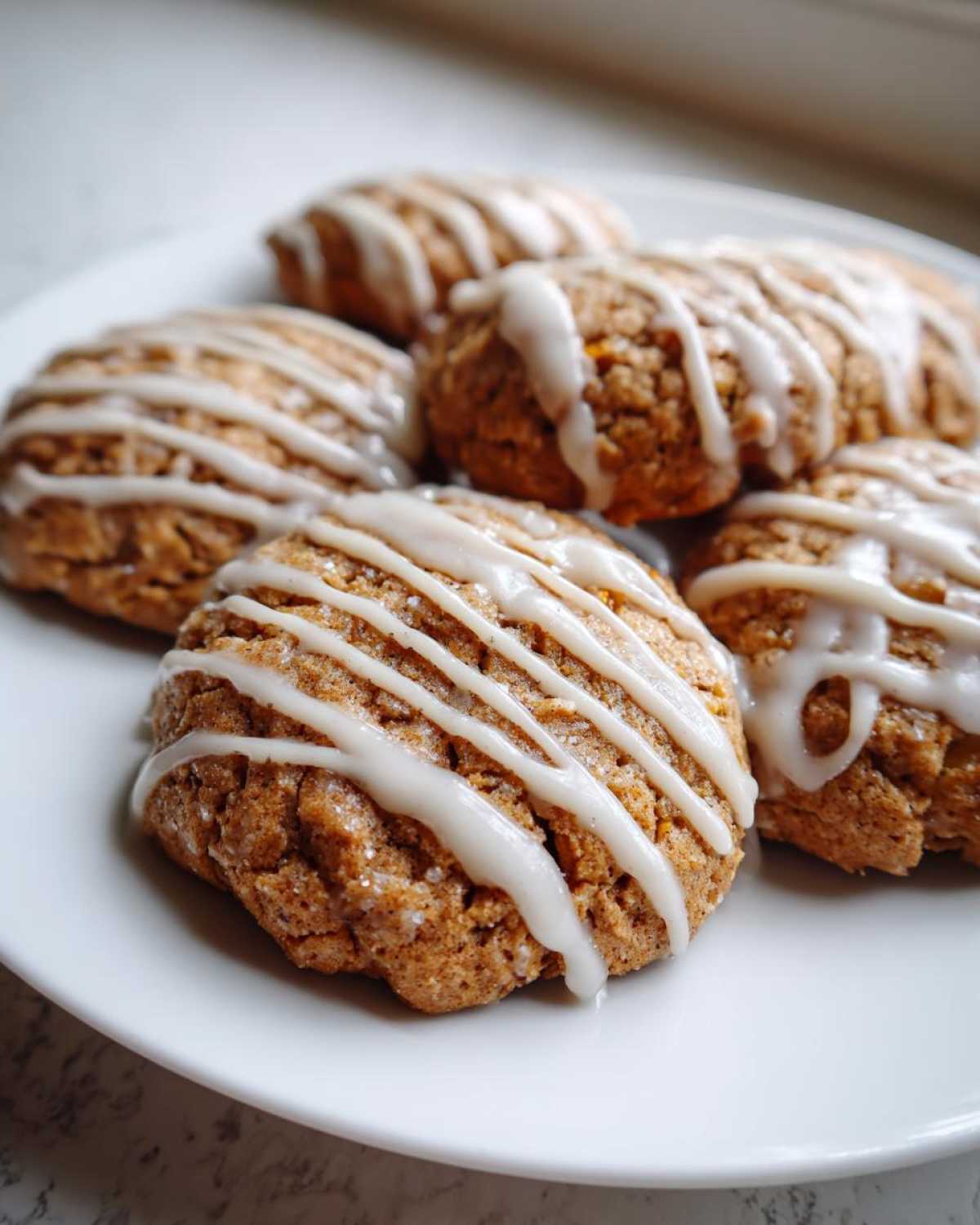 A close-up of several soft persimmon cookies drizzled with white vanilla icing on a white plate.
