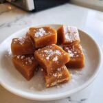 Close-up of soft, chewy caramels sprinkled with sea salt flakes, piled on a small white dish.