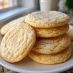 A stack of freshly baked, soft sugar cookie rounds dusted with sparkling sugar on a white plate.