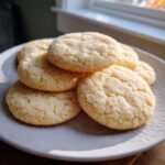 A stack of soft, round sugar cookie treats coated in sparkling sugar, illuminated by window light.
