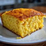Close-up of a golden, moist slice of sourdough cornbread on a white plate.