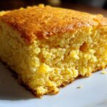A close-up, detailed shot of a moist, golden slice of sourdough cornbread on a white plate.