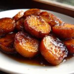 A close-up of thick-cut, glazed southern candied yams soaking in a rich, dark syrup on a white plate.