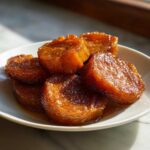Close-up of thick, glazed slices of southern candied yams piled on a white plate.