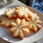 A pile of freshly baked, star-shaped butter cookies sprinkled with sugar on a white plate.
