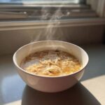 A steaming white bowl filled with hearty homemade cream of chicken soup, rich with shredded chicken.