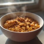 A close-up of a white bowl filled with thick, steaming homemade cream of chicken soup, rich with shredded chicken.