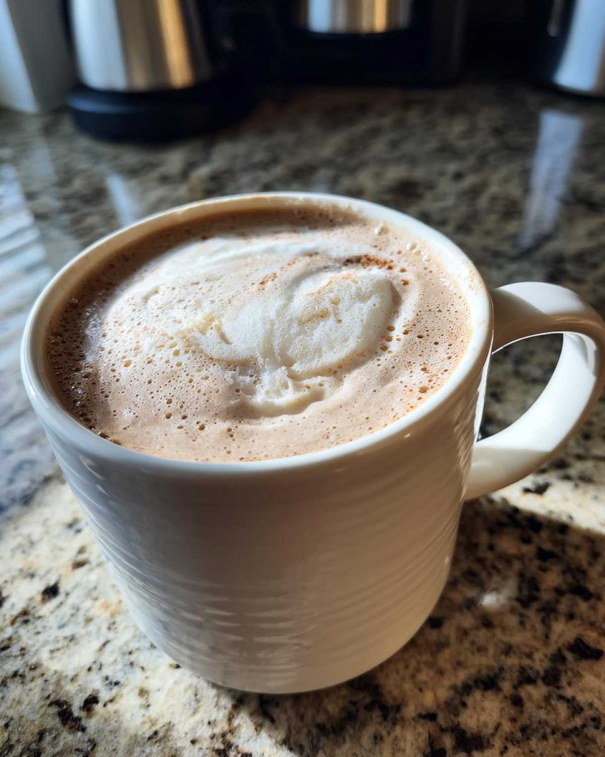 Close-up of a creamy white hot chocolate topped with foam and a sprinkle of spice in a white mug.