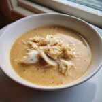 A close-up of a bowl of creamy crab soup generously topped with large flakes of white crab meat.