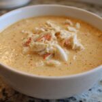Close-up of a creamy, orange-hued crab soup garnished generously with flakes of white and red crab meat.