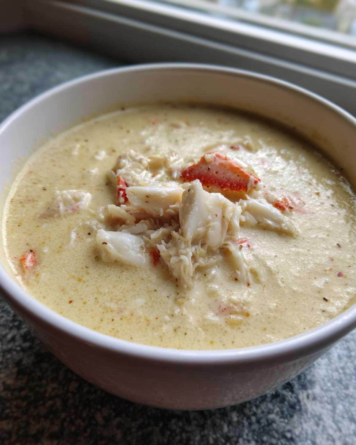 Close-up of a creamy, yellow crab soup garnished generously with large chunks of white and red crab meat.