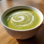 Close-up of velvety zucchini soup garnished with a swirl of cream and herbs.