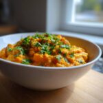 A close-up of a white bowl filled with vibrant orange pumpkin curry, topped generously with fresh, chopped cilantro.