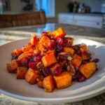 A close-up of a serving of vibrant sweet potato salad mixed with dried cranberries and pecans on a white plate.