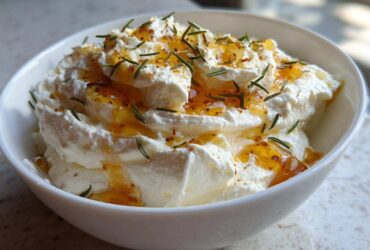 A close-up of creamy whipped ricotta dip with hot honey drizzled on top and garnished with fresh rosemary.