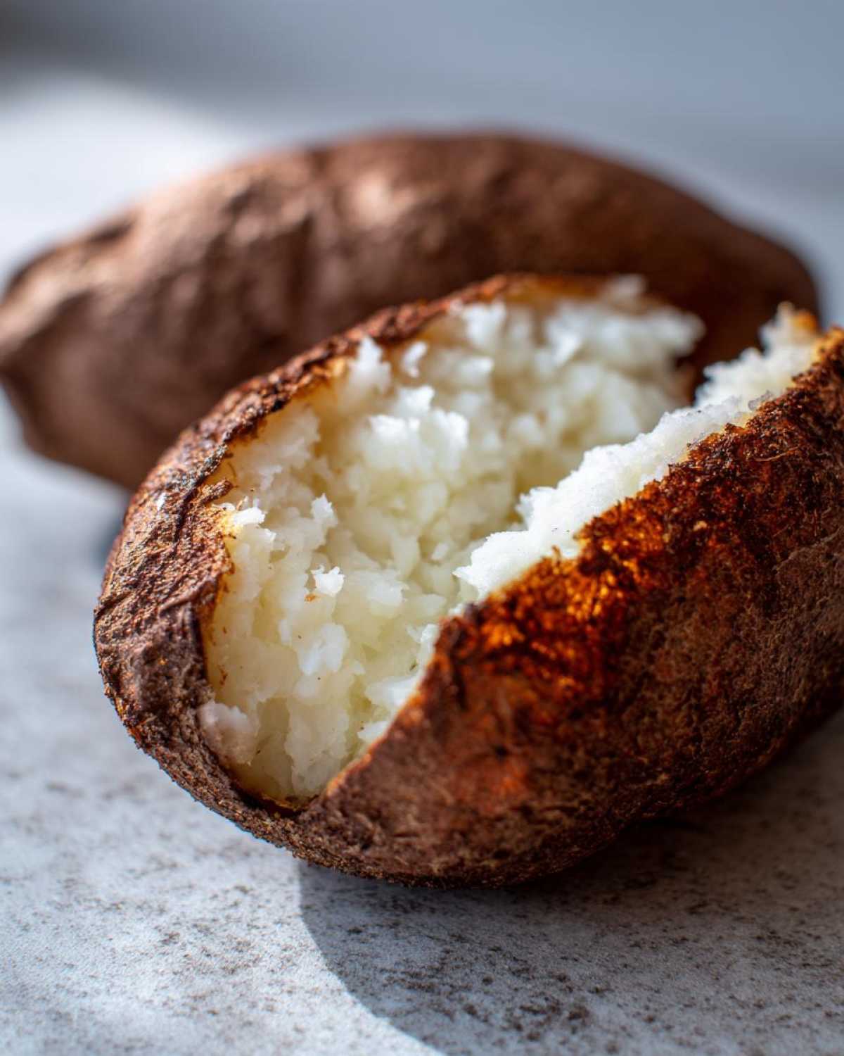 Close-up of a perfectly cooked air fryer baked potato split open to show fluffy white interior and crispy brown skin.