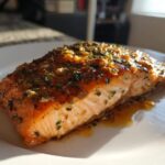 Close-up of a perfectly cooked air fryer salmon fillet topped with a glossy glaze of herbs and garlic.