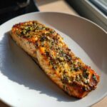 Close-up of a flaky, seasoned fillet of air fryer salmon resting on a white plate.