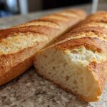 Close-up of a freshly baked french bread baguette, showing a golden, scored crust and the soft interior crumb.