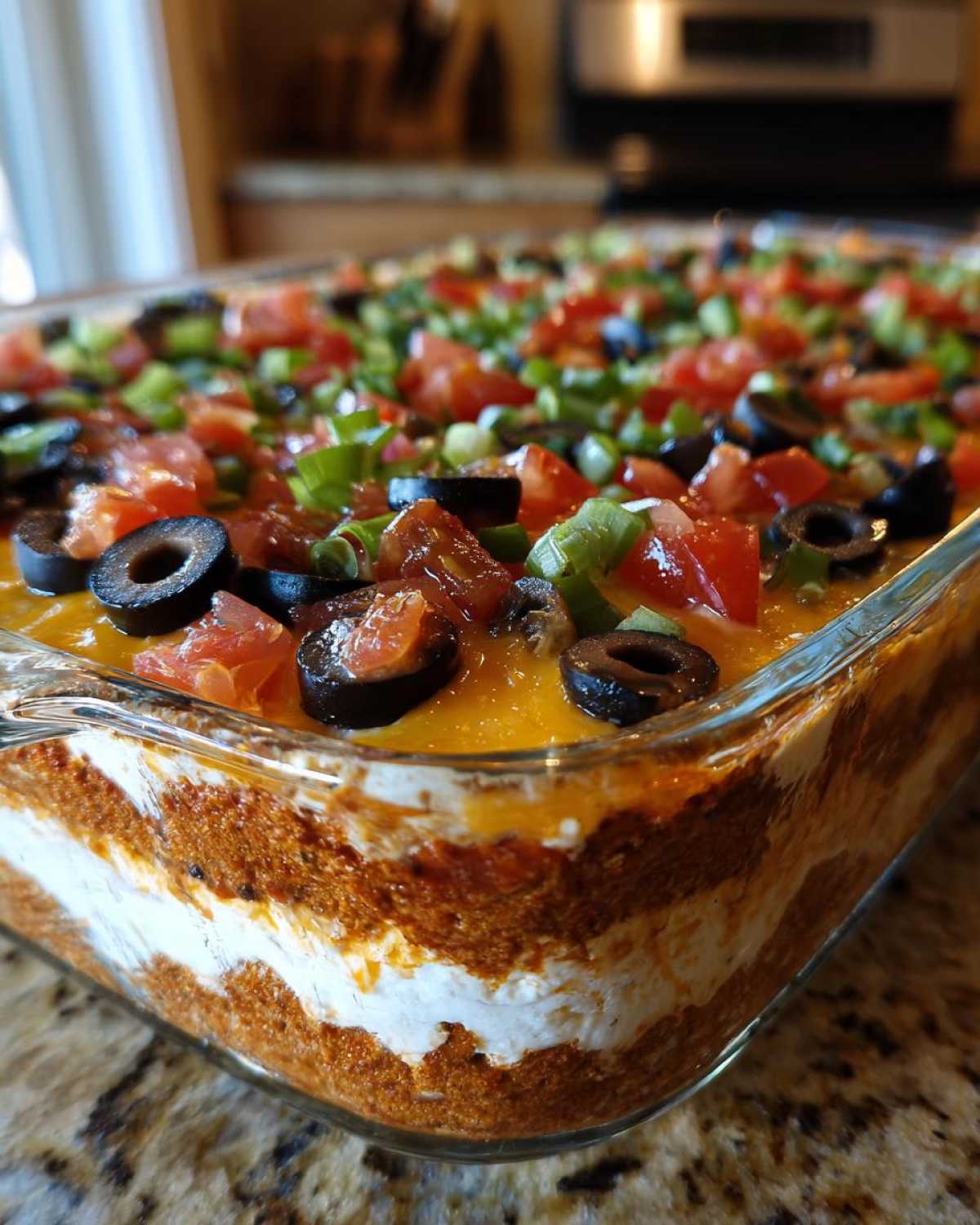 Close-up side view of a glass dish filled with a vibrant 7 layer dip, showing distinct layers and toppings of olives, tomatoes, and green onions.