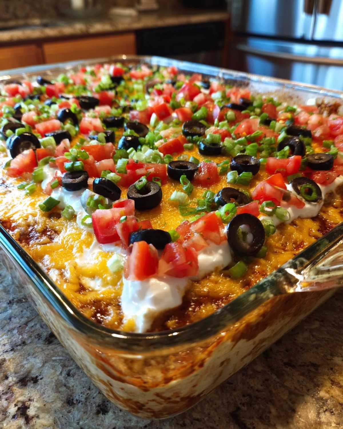 A close-up of a fully assembled 7 layer dip topped with melted cheese, sour cream, olives, tomatoes, and green onions.