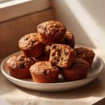 A stack of freshly baked bran muffins, one broken open to show the texture and raisins inside.