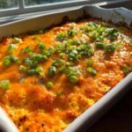 Close-up of a freshly baked Buffalo chicken dip topped with melted orange cheese and chopped green onions.