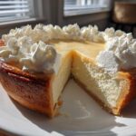 A rich, golden-crusted butterscotch pie with a slice removed, topped with swirls of white whipped cream.