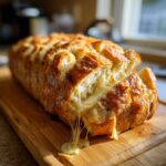 Close-up of freshly baked, pull-apart cheese bread on a wooden board with melted cheese strings stretching out.