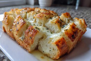 Close-up of a baked, pull-apart style cheese bread loaf with melted mozzarella and herbs.
